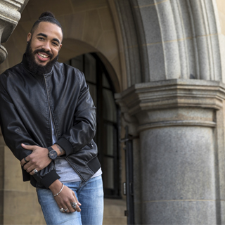 Student wearing a black jacket standing in front of a stone arch in Bradford