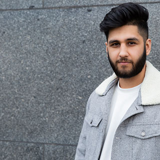 A University of Bradford student stood in front of a dark grey stone wall