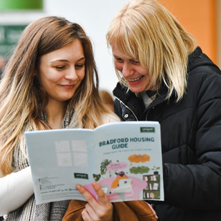 Two people, one younger and one older, smiling and looking at a booklet that says Bradford Housing Guide 