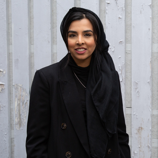 A University of Bradford student wearing a hijab stood in front of a white paneled wall