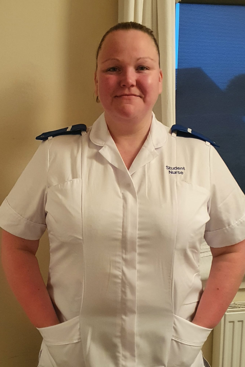 A woman wearing a white nurse's uniform looks at the camera while smiling.