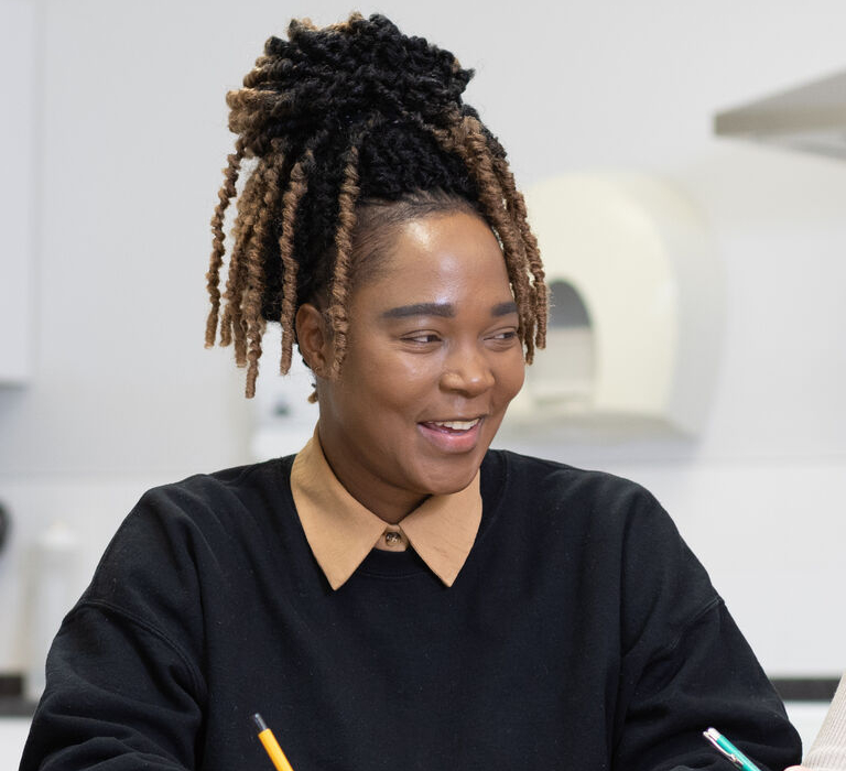 Three smiling women sit at a table with pens in hand