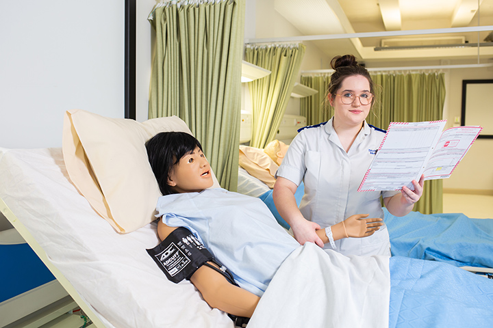 A student nurse looking at charts working on a patient doll