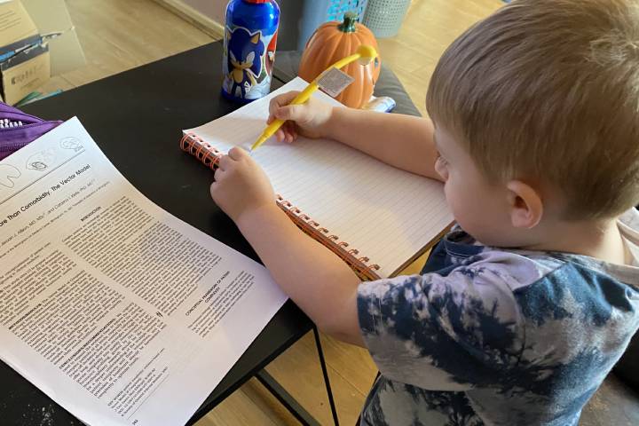 A child sits at a desk while writing in a large notebook.