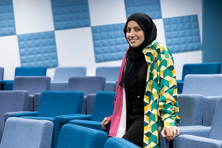 A student standing in an empty lecture theatre smiling at the camera