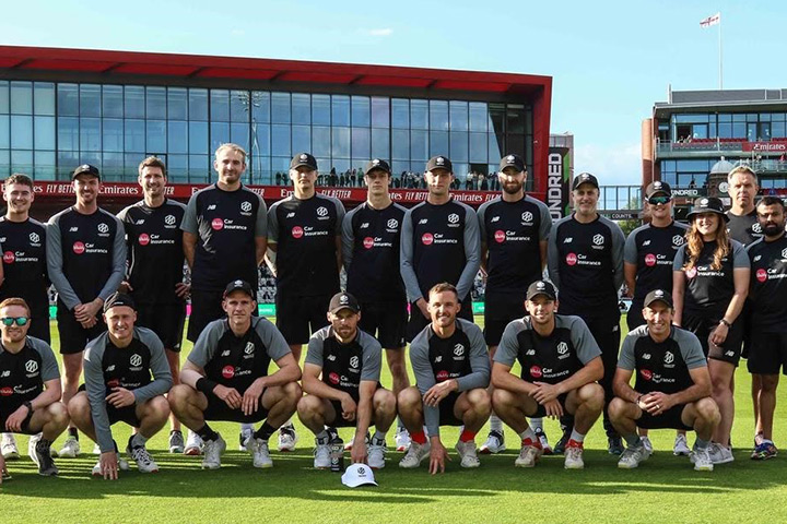 A student poses for a picture with cricket team at a cricket stadium on the grass pitch