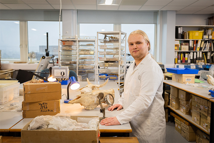 A student in a lab wearing a labcoat smiling at the camera