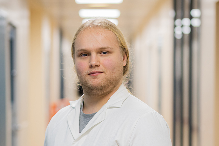 A student wearing a lab coat smiling at the camera