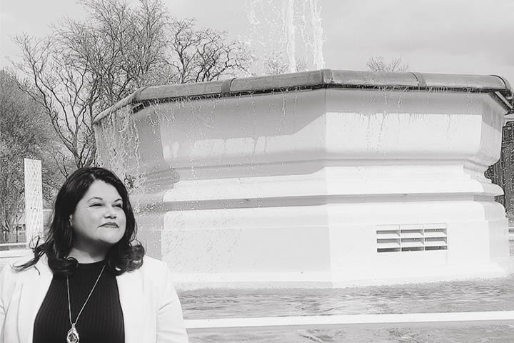 A student looks into the distance as they are standing to the left hand side of an active fountain