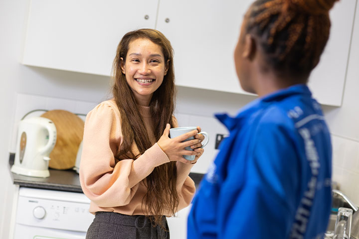 Two students standing in a kitchen, chatting and drinking tea.