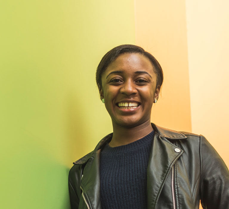 A student smiling at the camera and leaning against a wall.