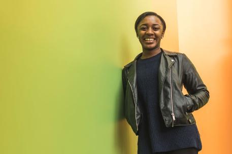 A student smiling at the camera and leaning against a wall.