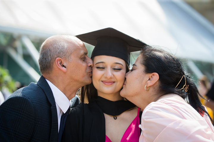 A graduate with a parent or carer on either side kissing their face