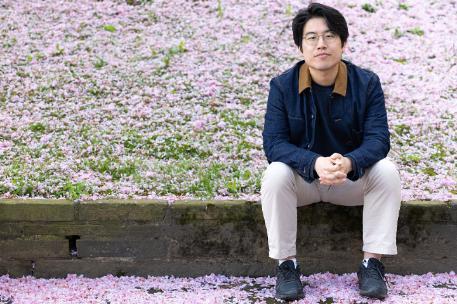 A student sitting on a low wall with cherry blossoms in the background