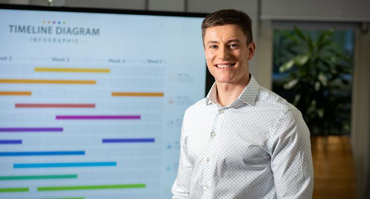 A student standing in front of a board smiling at the camera.