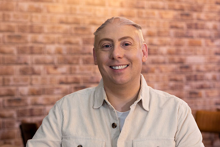 A student smiling at the camera in front of a brick wall in the background