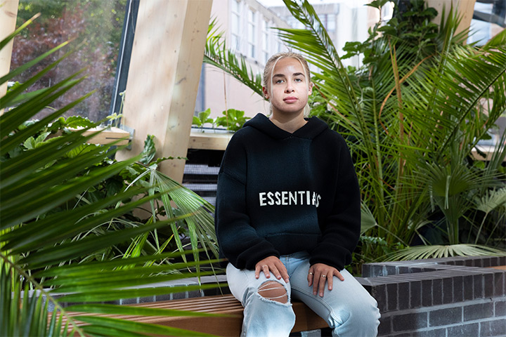 A student sitting on a wall in front of indoor plants