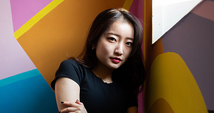 A postgraduate student posing in a colourful room on campus