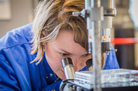 An image of a female technician looking into a microscope