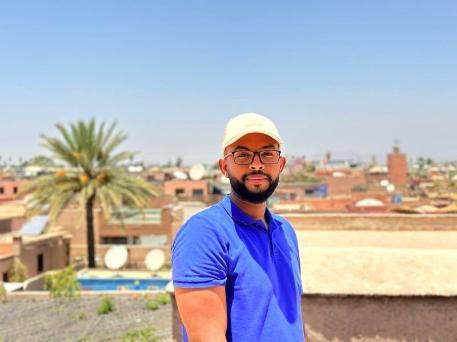 Ali Maysara, MSc Big Data Science and Technology, 2021 wearing a white hat and blue shirt on a summers day.