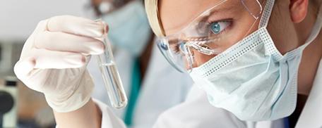 A scientist wearing a mask looking at a test tube experiment