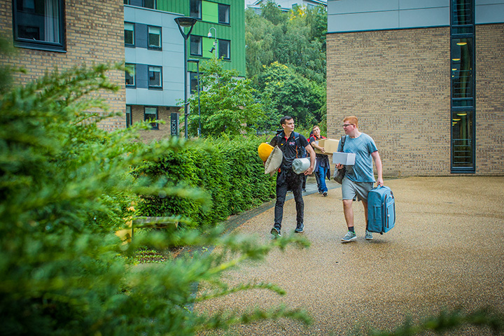 Three students walking into the Green accommodation with luggage