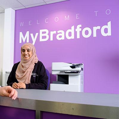 Person sat in front of a purple background, with the sign that reads, 