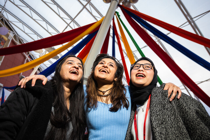 Three people smiling under rainbow coloured ribbons hung from the ceiling of the Richmond Building Atrium.