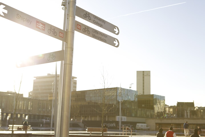 Image of buildings in Bradford and a signpost indicating the direction of travel from the city centre for Shipley, the University and College, and Little Horton and Marshfields.