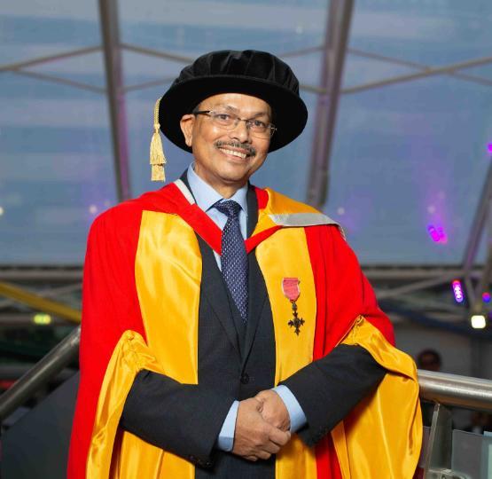 Person in graduation gown stands by barrier in atrium having picture taken