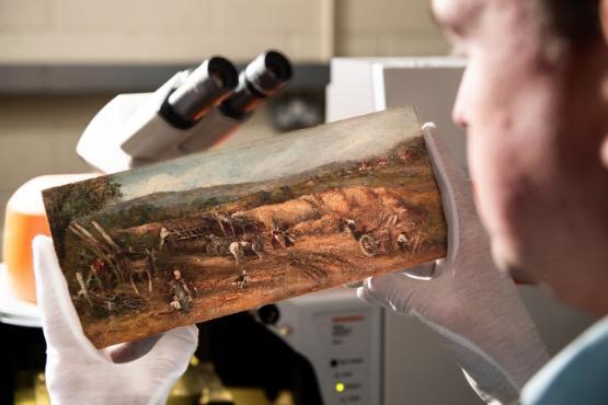 Close up photo of an oil painting underneath a microscope being held by a university staff member