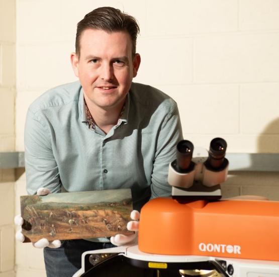 Staff member holds small oil painting next to scientific equipment