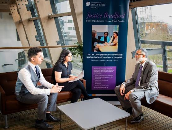 three people sat talking in buisness school building at university with table in the middle of them