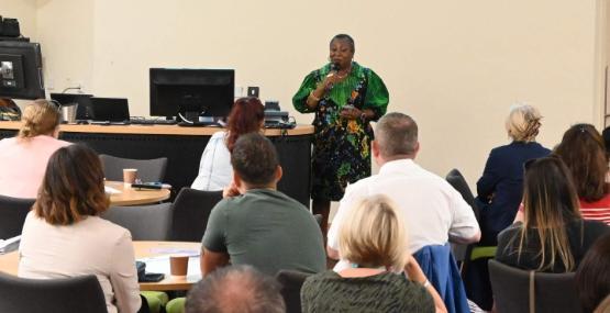 A University of Bradford staff member stands up and speaks to a room full of people sat at tables at an event