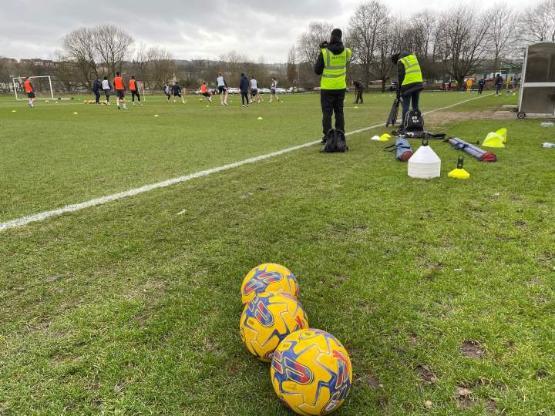 two students in hi-vis jackets filming football training session