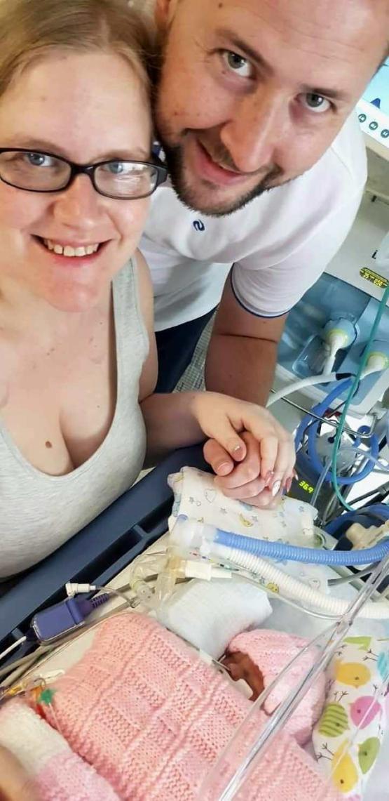 Two people standing up with baby in front of them in a hospital