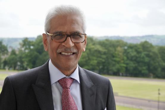 University staff member wearing suit and tie close up to camera with fields and trees behind them