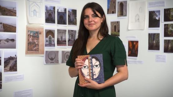 a person holds a book while in an art gallery with a number of pictures hanging on the wall behind them