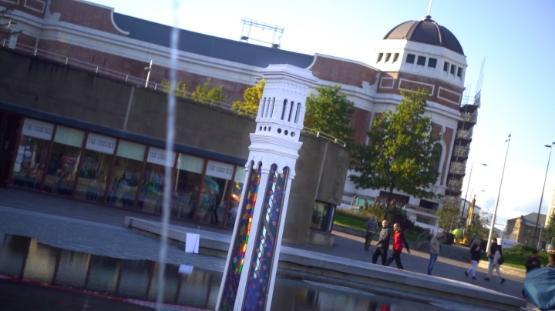 An large art installation is in a small water pool in a city centre with large buildings behind it