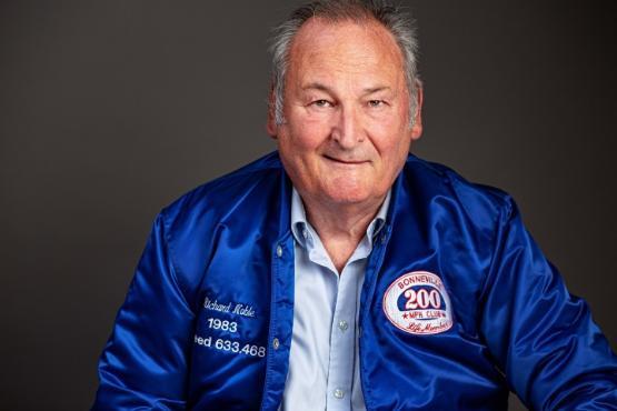 Close up photo of a person wearing a blue bomber type jacket smiling at the camera