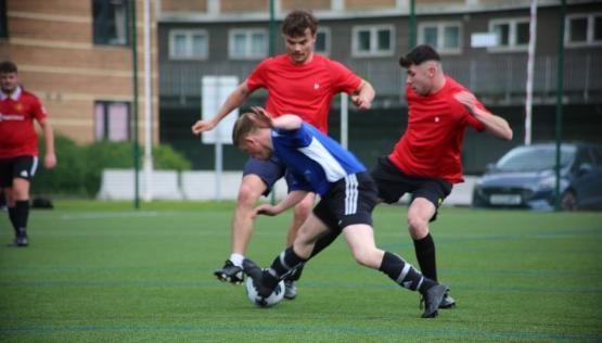 A football player in a blue shirt is falling onto the ground as two players in red shirts tackle them