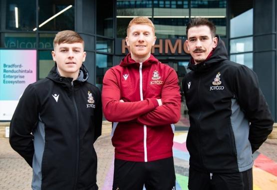 Three football players wearing tracksuits stood up outside university entrance