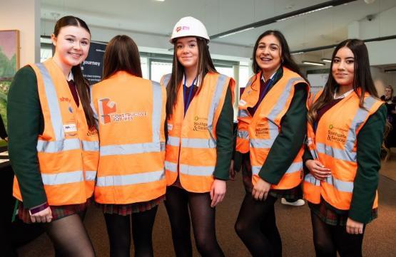 A group of five students stood up wearing orange hi-vis jackets and hard hats