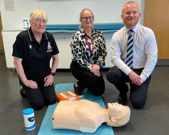 three people on their knees with a CPR dummy in front of them