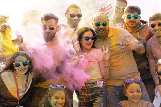 A group of students smiling and covered in pink and orange dusty paint at a party