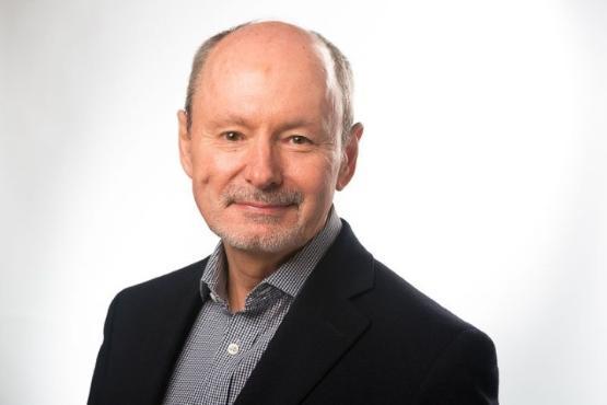 Head of shoulders photograph of a person who is wearing a black suit jacket and collared shirt