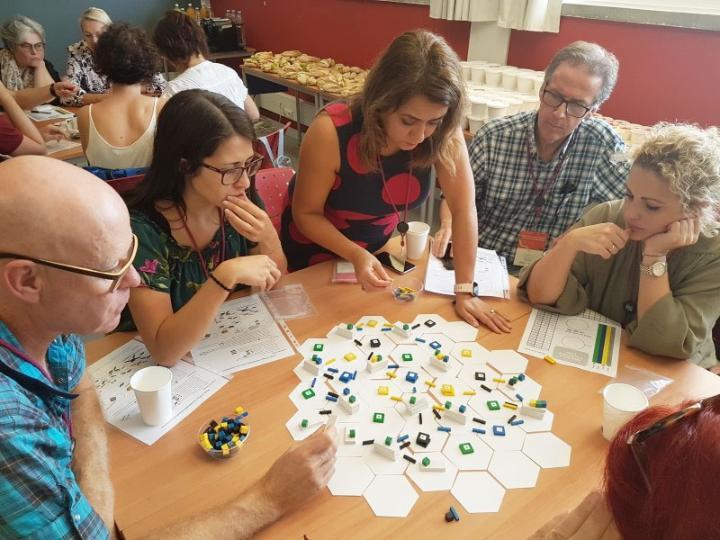 Educators around a table as Dr Sara Rye demonstrates her game based learning techniques