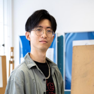 A student with black hair and glasses looks into the camera.