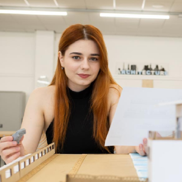 A student with red hair looks into the camera with a table in front of them.