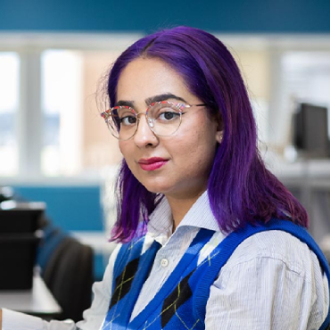 A student with purple hair looks at the camera while using a piece of engineering equipment.